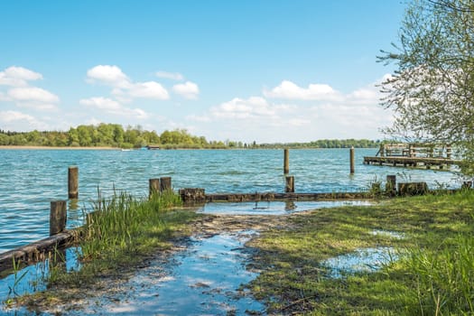 Flooded shore of Chiemsee, Germany, in bright sun with blue sky and white clouds