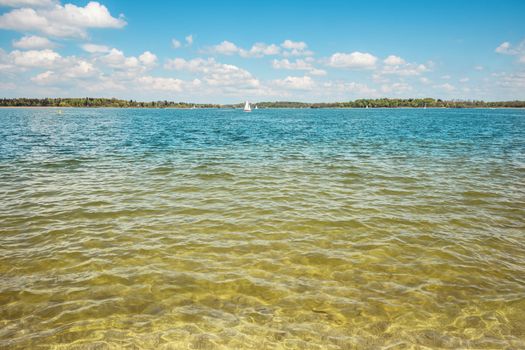 Water of the lake Chiemsee in Germany with bright sun, blue sky and white clouds