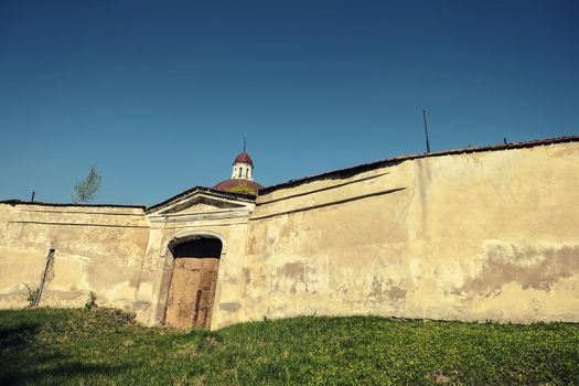 Monastery on the green hill with closed gate in a high wall