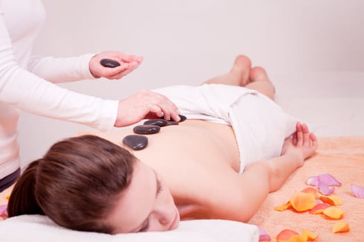 young attractive woman get hot stone massage by professional in wellness spa salon