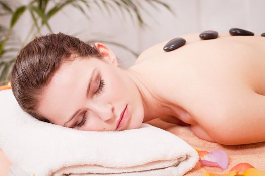 young attractive woman get hot stone massage by professional in wellness spa salon