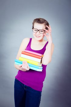 Silly smiling schoolgirl with glasses and lots of books having fun