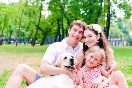 Happy young family with Labrador is resting in the park