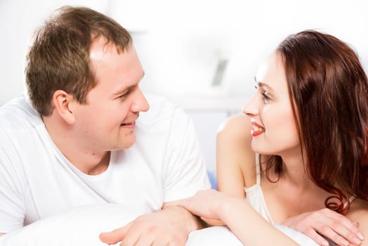 Young man and woman lying together in bed, smiling and happy