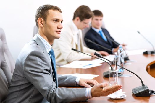 Portrait of a businessman, said into the microphone, in the background colleagues communicate with each other