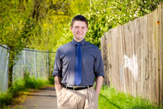 A college student business professional is photographed outside with natural light to create a portrait of a person wearing a grey shirt looking confident.