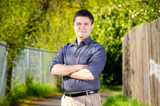 A college student business professional is photographed outside with natural light to create a portrait of a person wearing a grey shirt looking confident.