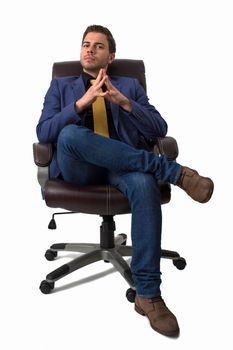 Young thoughtful businessman sitting on a chair wearing a blue suite with jeans and a golden tie