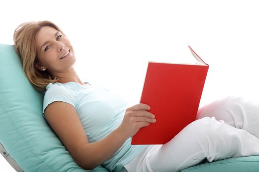 Smiling woman relaxing on a comfortable recliner or day bed reading a large red book isolated on white