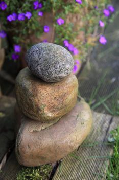 Stack of three different natural garden stones with weatherworn smooth surfaces standing on a wooden deck in the garden