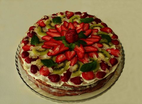 cake with cream filling covered with strawberries kiwi and mint green and almonds. close to