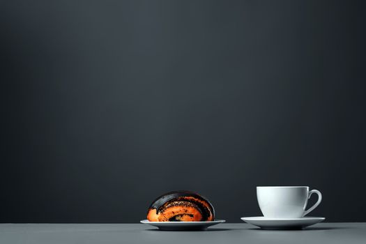 White mug and a chocolate muffin with poppy seeds on a gray background.