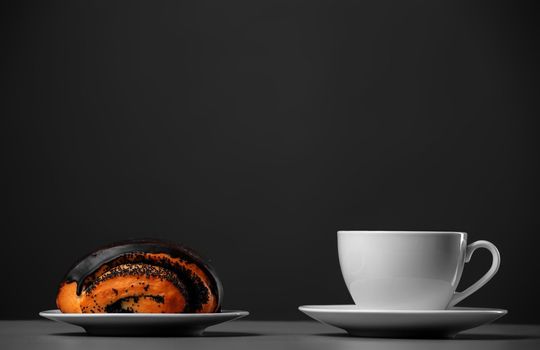 White mug and a chocolate muffin with poppy seeds on a gray background.