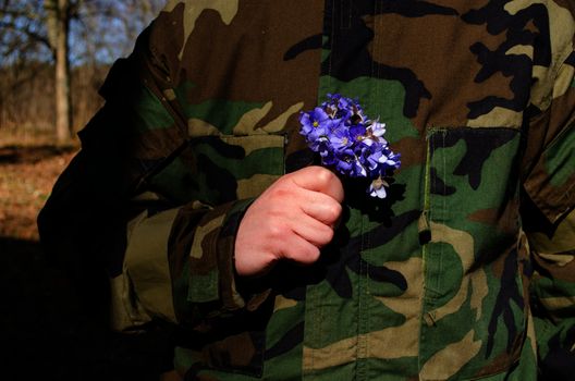 soldier in camouflage wear hold violet flowers in hand picked for his wife girlfriend. back from army.