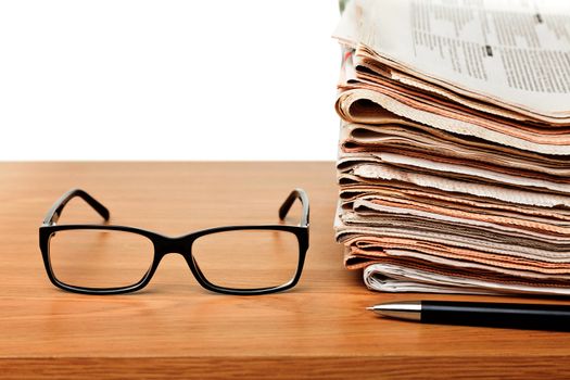 News concept — glasses on a table with stack of newspapers