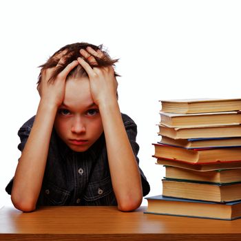 Portrait of upset schoolboy sitting at desk with books holding his head