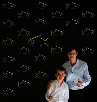 Thumbs up boy dressed up as business man with teacher man and independent thinking chalk fish swimming against the flow on blackboard background