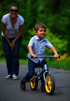 Little boy on a bicycle and his mother in the summer park