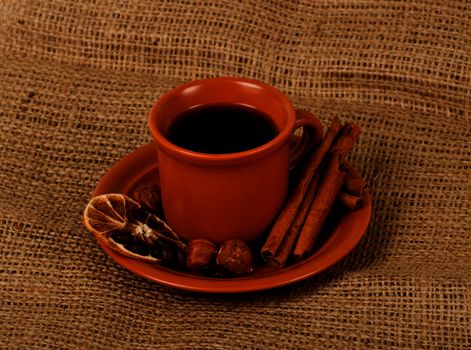 Closeup shot of freshly prepared cup of italian espresso with cinnamon, coffe beans, nuts and lemon over sacking