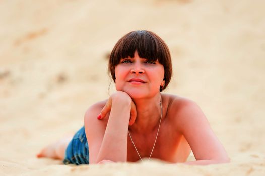 Girl in denim shorts tan while lying on the sand