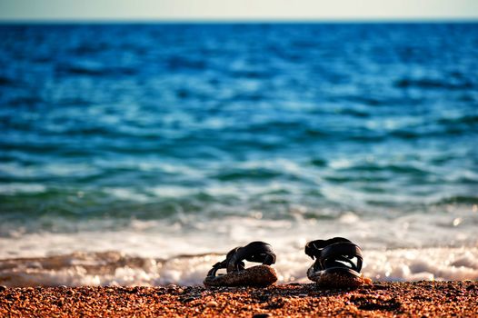 Beach shoes at the edge of the sea on the sandy beach.