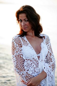 Portrait of a beautiful girl in a white shawl on the beach.