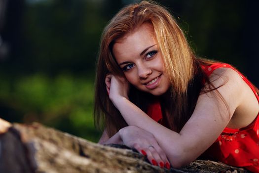 Beautiful girl in a red dress, lying on a log