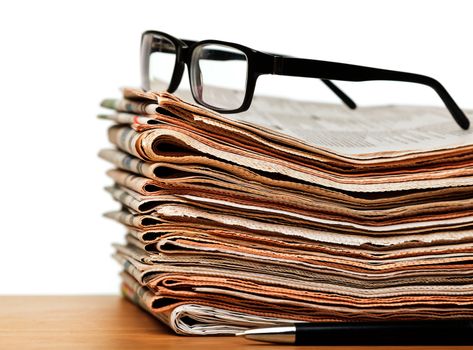 News concept — glasses on a stack of newspapers with pen