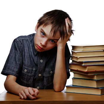 Portrait of upset schoolboy sitting at desk with books holding his head