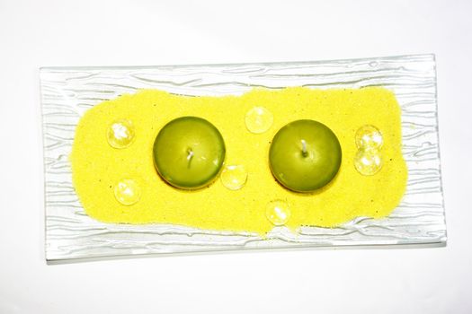 two green candles on yellow sand with glass gobs