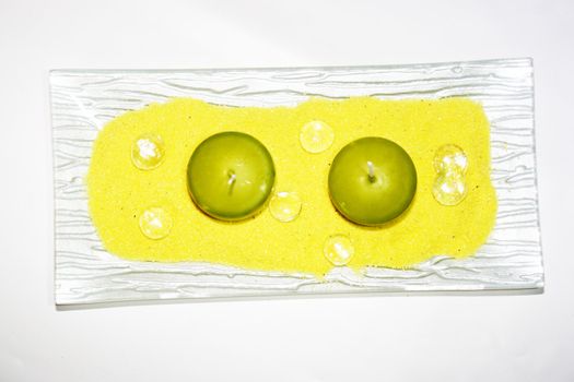 two green candles on yellow sand with glass gobs