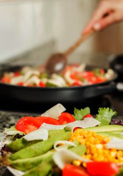 Closeup of fresh salad dish and female cooking in a black pan in the background