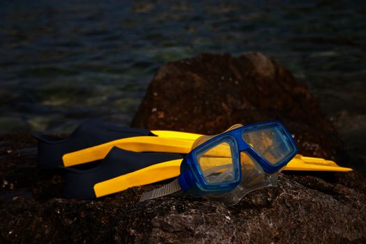 Yellow flippers with snorkel goggle on a rock near the sea