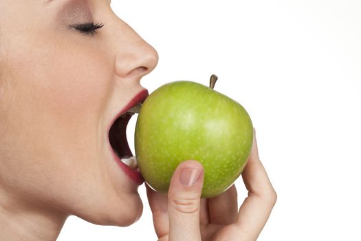 The apple is emphasised in the closeup studio shot of a women about to bite into an fresh apple.