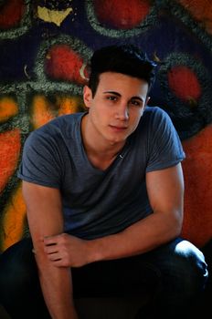 Attractive young man sitting outdoors in front of graffitti covered wall