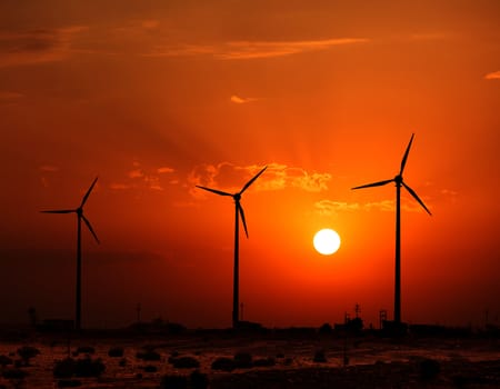 Green renewable energy concept - wind generator turbines sihouettes on sunset