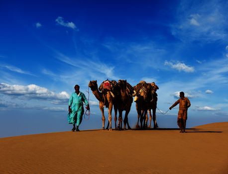 Rajasthan travel background - two Indian cameleers (camel drivers) with camels in dunes of Thar desert. Jaisalmer, Rajasthan, India