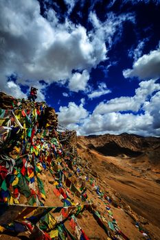 Travel photographer taking photos in Himalayas mountains on cliff with Buddhist prayer flags. Leh, Ladakh, Jammu and Kashmir, India