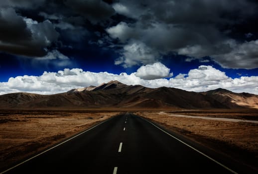 Travel forward concept background - road on plains in Himalayas with mountains and dramatic clouds. Manali-Leh road, Ladakh, Jammu and Kashmir, India