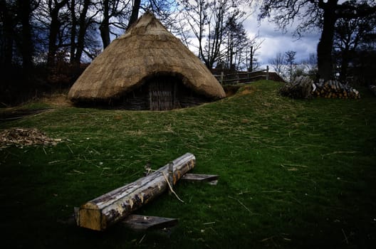 A replica of an iron age round house with log in foreground