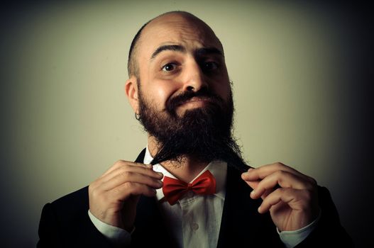  funny elegant bearded man touching beard on vignetting background