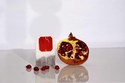 Juicy pomegranate and tea bag on white background