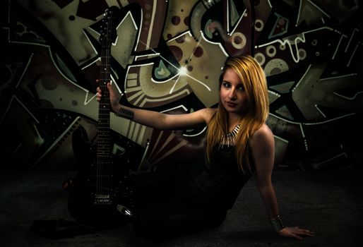 Young blonde holding a black guitar, over grafitti background