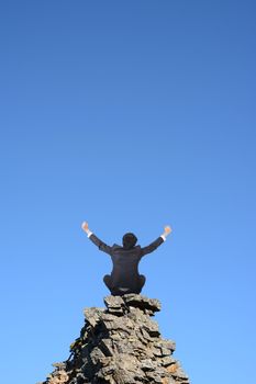 Businessman sit on rock and open arms against blue sky. Concept about freedom, struggle, relax and lifestyle etc.