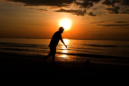 silhouette man playing soccer on the beach