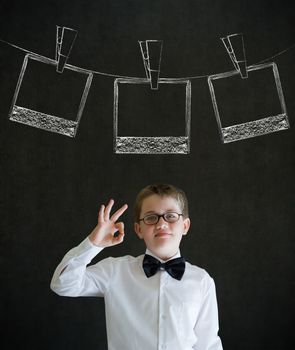 All ok or okay sign boy dressed up as business man with hanging instant photograph on blackboard background