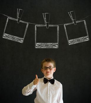 Thumbs up boy dressed up as business man with hanging instant photograph on blackboard background