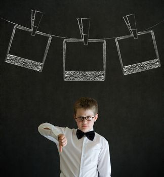 Thumbs down boy dressed up as business man with hanging instant photograph on blackboard background