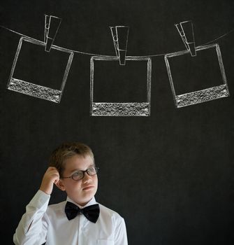 Scratching head thinking boy dressed up as business man with hanging instant photograph on blackboard background