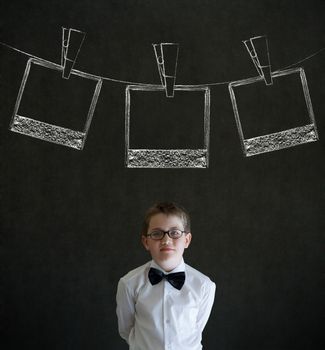 Thinking boy dressed up as business man with hanging instant photograph on blackboard background